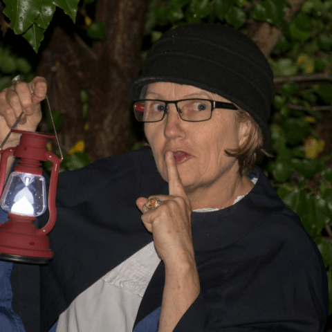 Sharon whispering to the audience holding a lantern